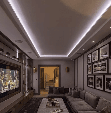 A home cinema room with backlit ceiling coving, a wall-mounted screen and ceiling speakers